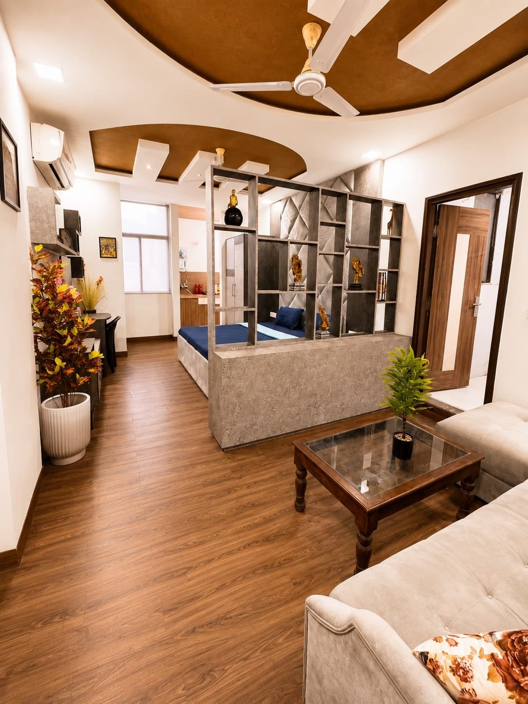 Studio with wooden floors, a sofa and coffee table, and an open shelf divider screening the bed