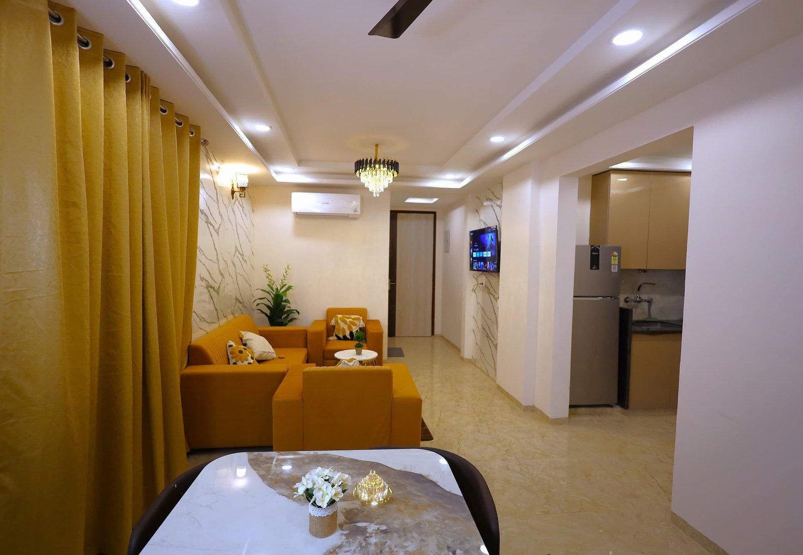 Open-plan living room with mustard sofas, gold curtains and the kitchen beyond