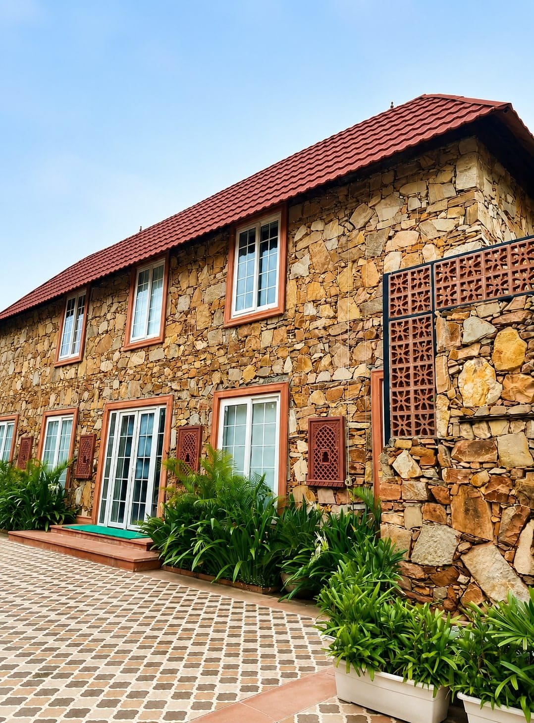 Stone villa with a red tiled roof and planters along patterned paving