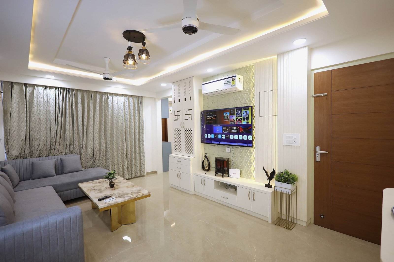 Living room with a grey sectional, a TV unit with lit shelving and sheer curtains