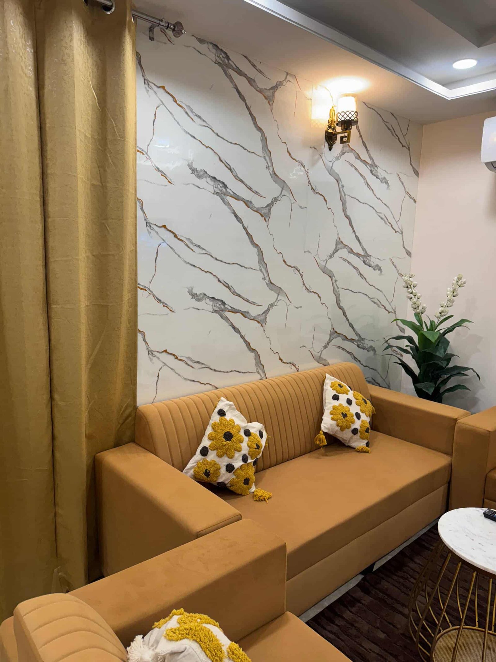 Mustard sofa with patterned cushions against a marble-effect feature wall