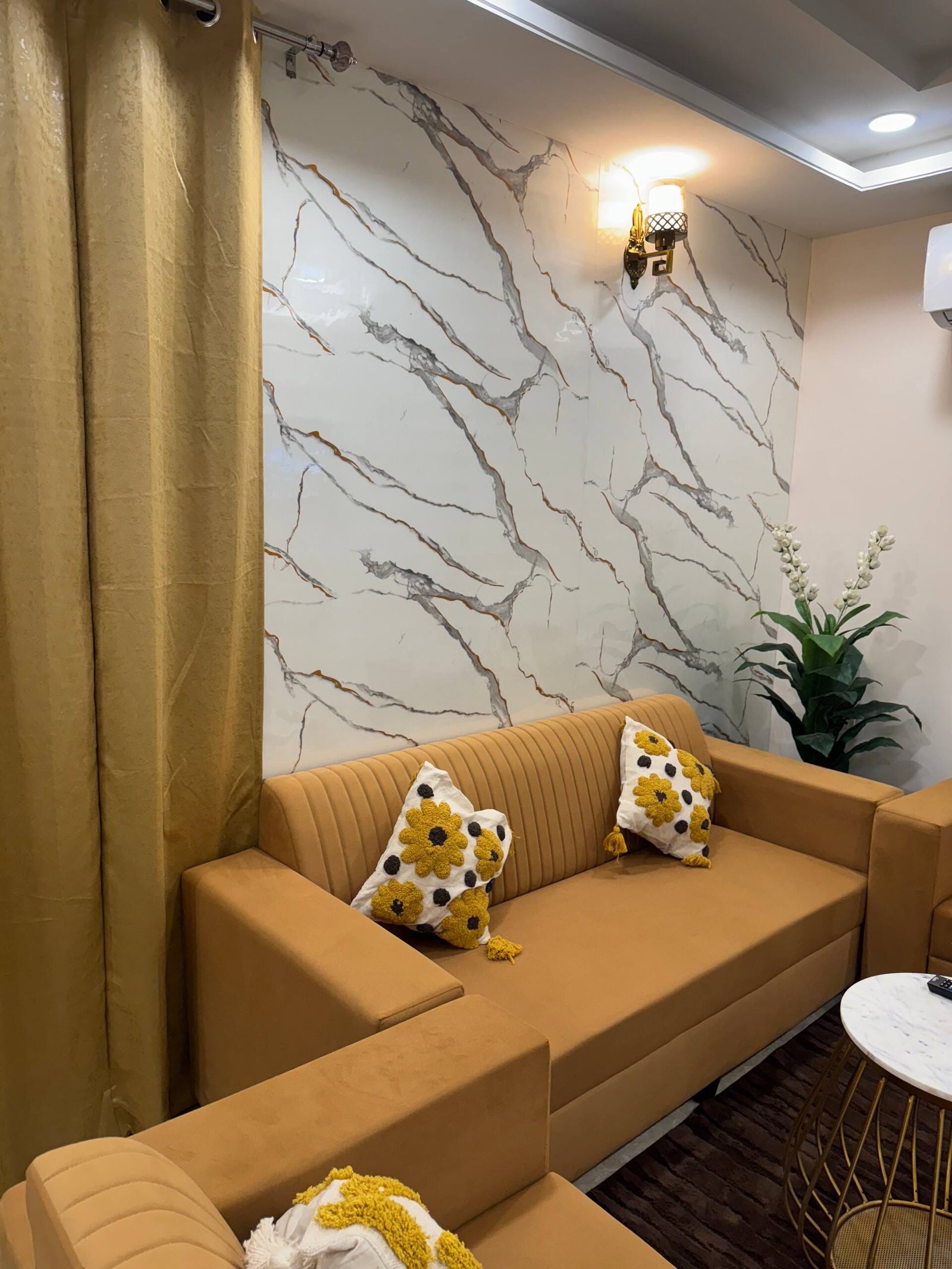 Mustard sofa with patterned cushions against a marble-effect feature wall
