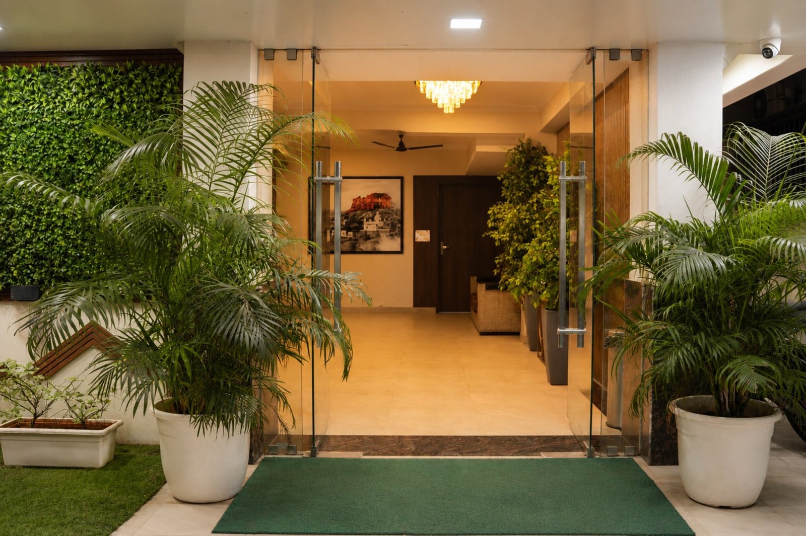 Glass entrance doors between potted palms, with the lit lobby beyond