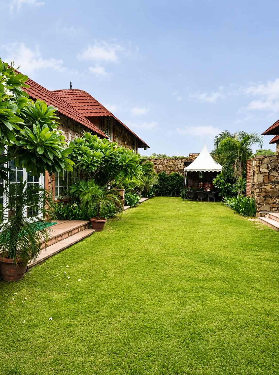 Lawn along the stone villas, bordered by trees, with a white gazebo at the far end