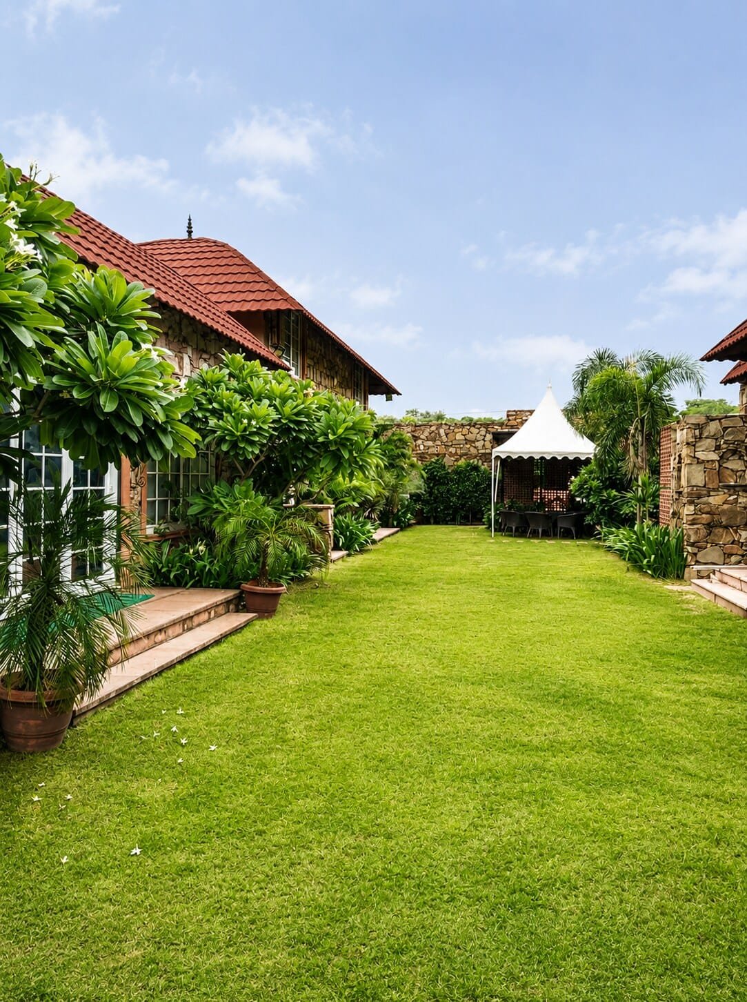 Lawn along the stone villas, bordered by trees, with a white gazebo at the far end