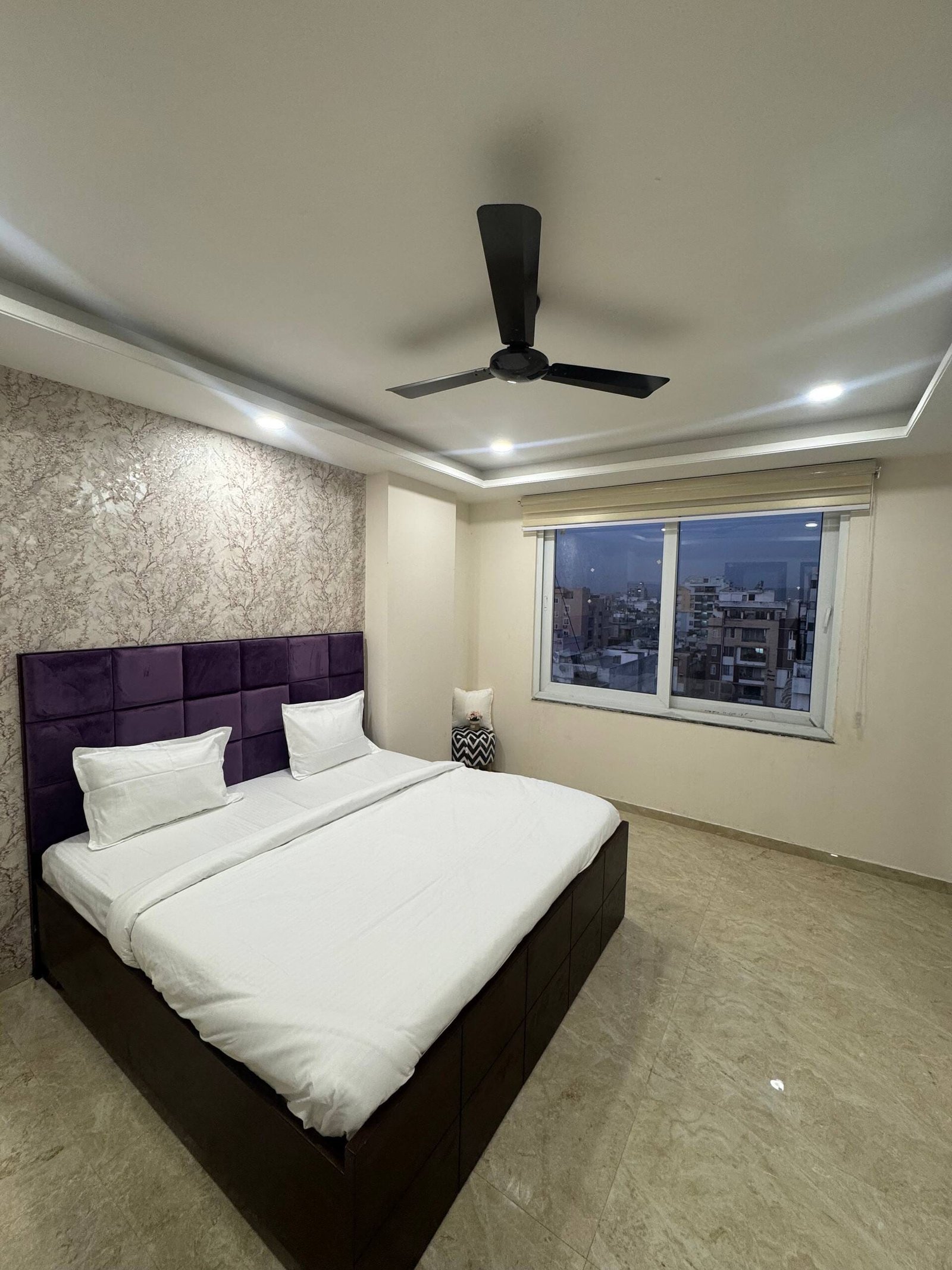 Bedroom 1 with a purple tufted headboard and a window over the city