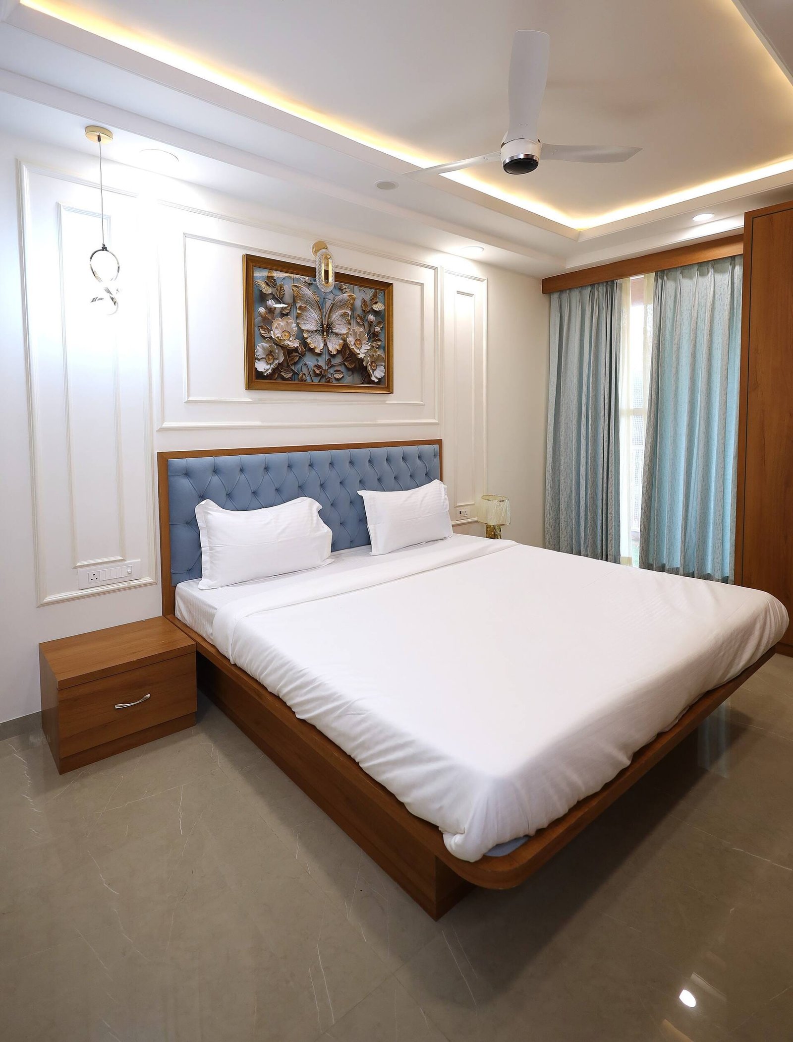 Bedroom 1 with a tufted blue headboard, white linen and framed artwork