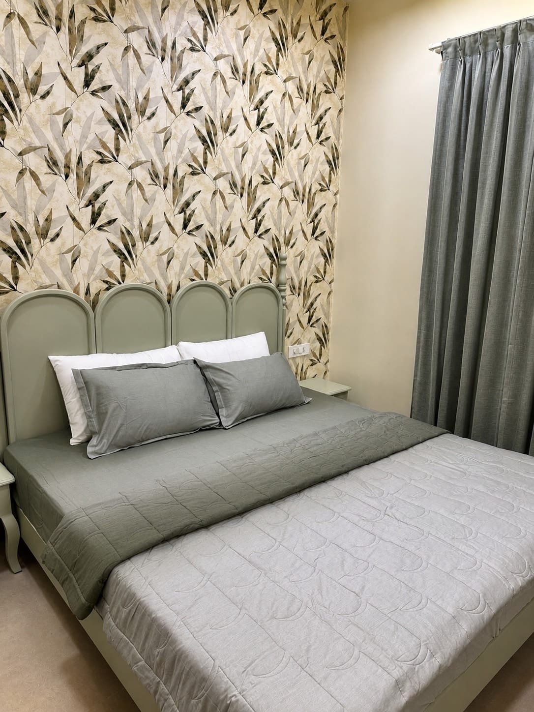 Bed with a grey quilt and a scalloped green headboard