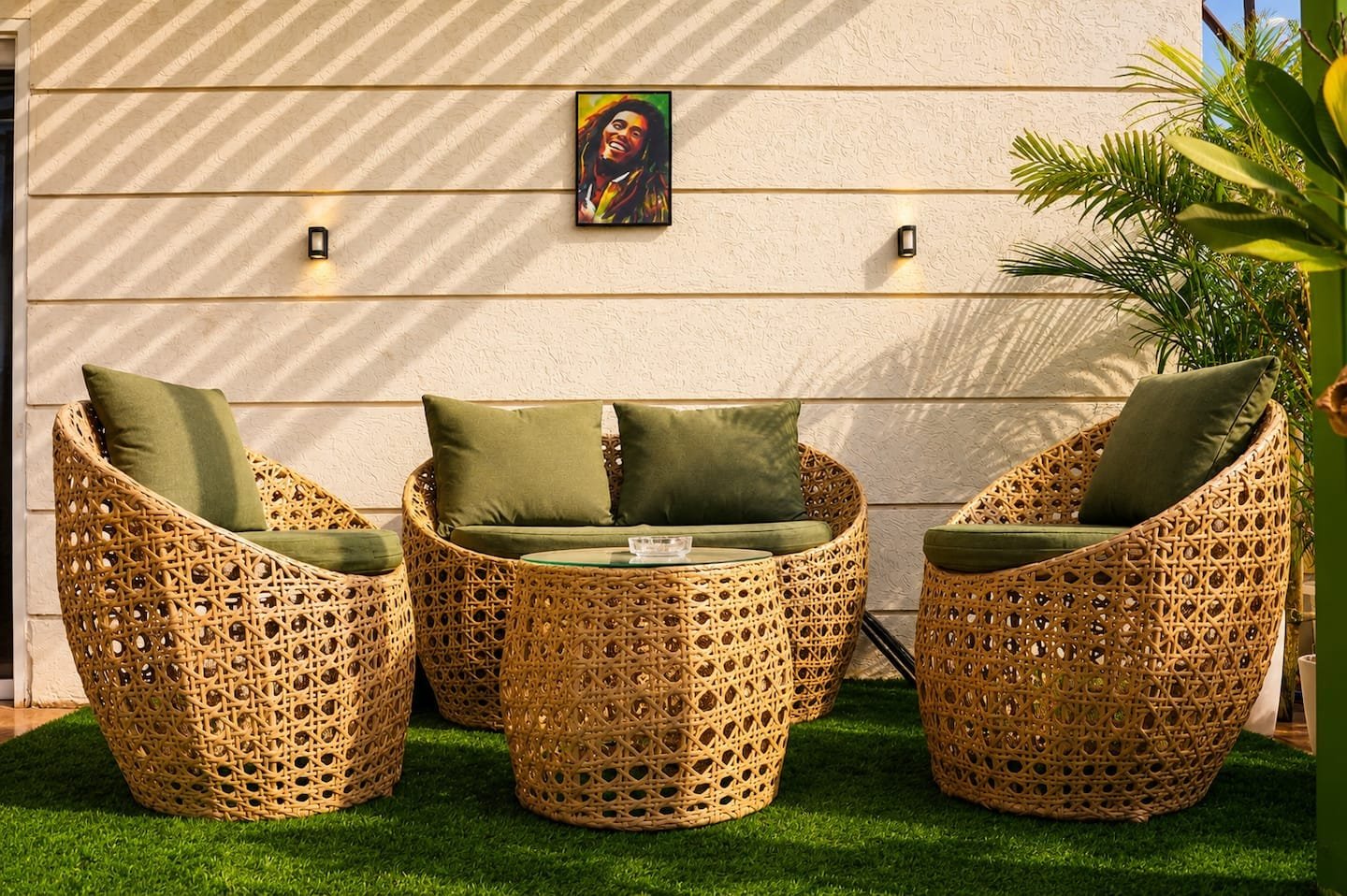 Three wicker chairs with green cushions on artificial grass