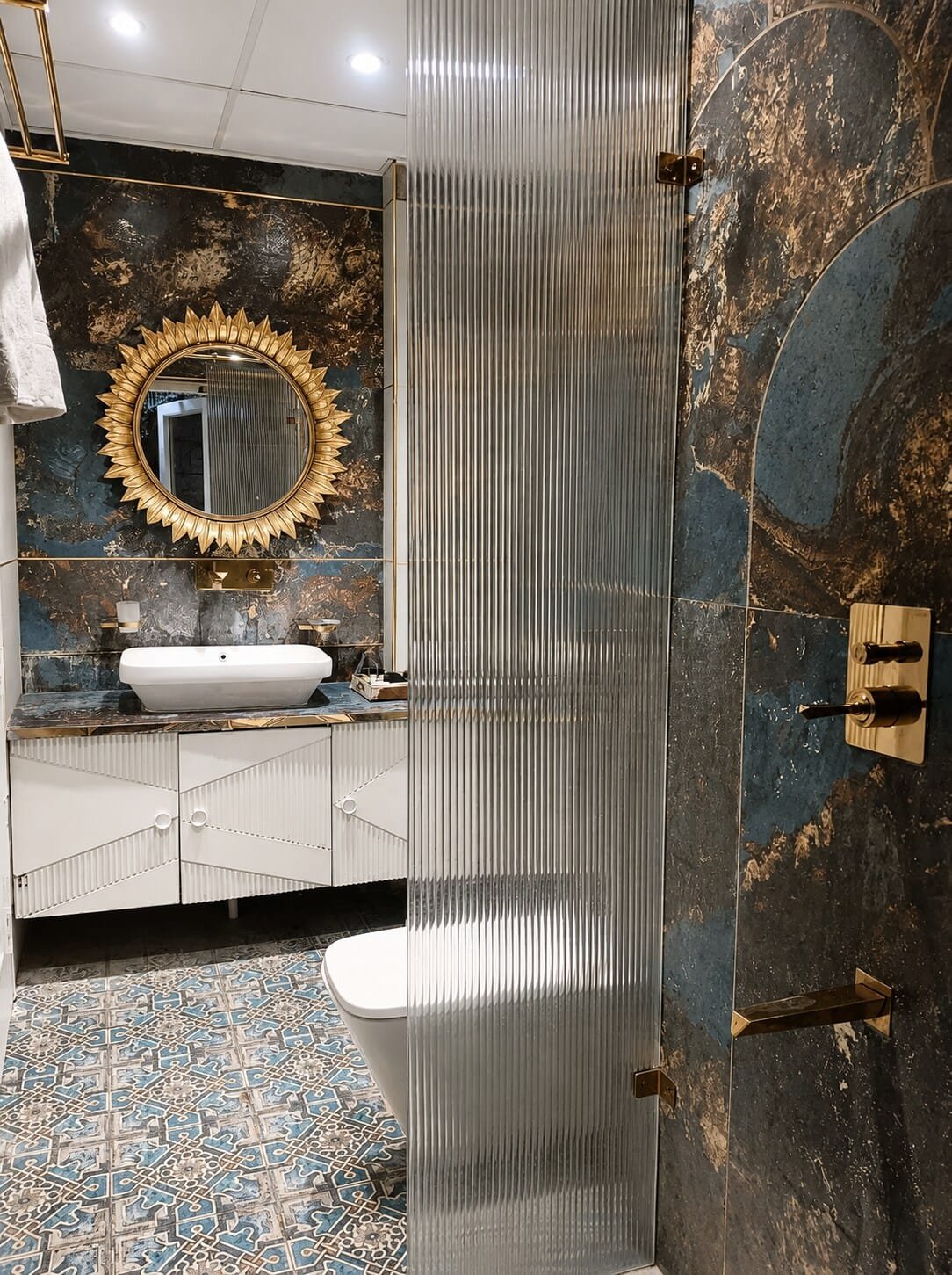 Bathroom with a gold sunburst mirror, vessel basin and dark marble wall