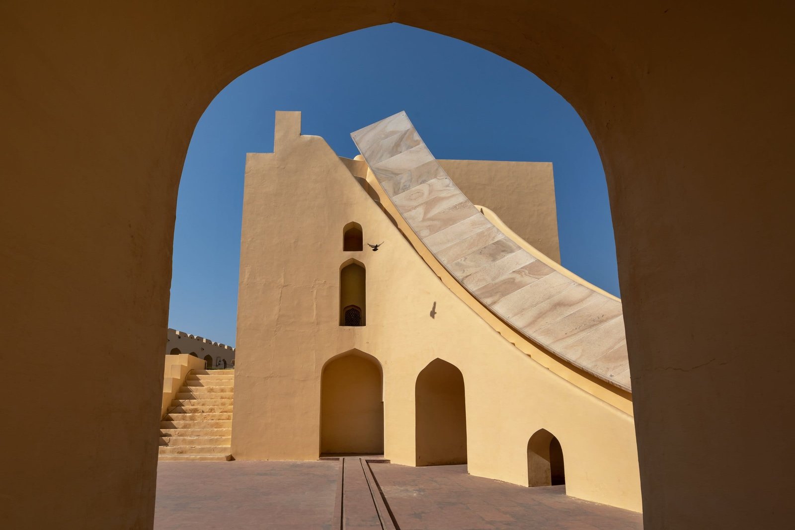 A curved stone instrument at Jantar Mantar framed by an arch