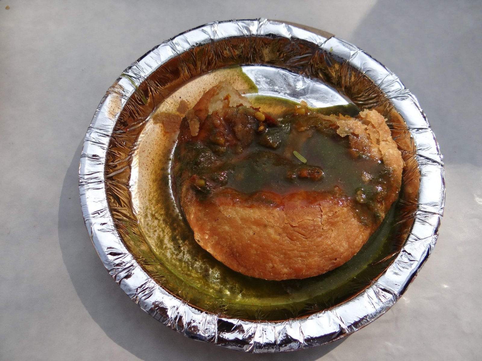 A pyaaz kachori broken open on a foil plate, with tamarind chutney